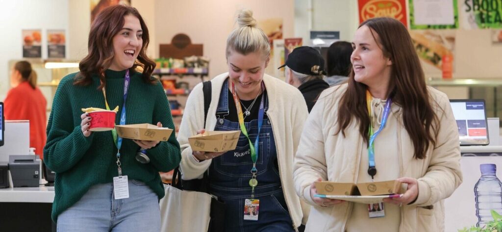 Three students in the canteen walking towards the camera with their breakfast