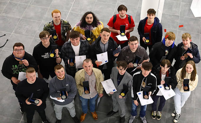 A large group of Cambria World Skills winners all holding their medals looking up towards the camera