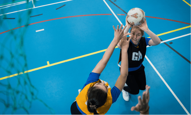 A netball player about to throw a netball whilst another player attempts to block the shot