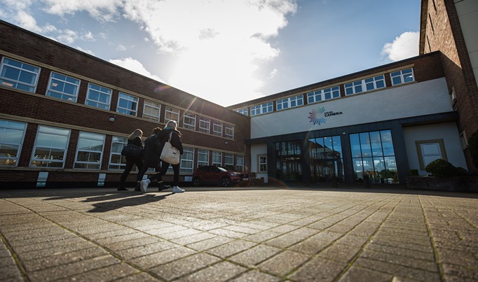 A group of three college students walking into the Deeside College site through the main entrance in the reception area