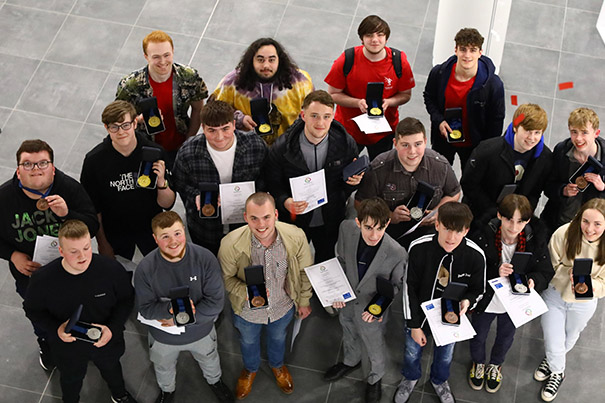 A group of smiling students all looking upwards holding medals from the World Skills competition