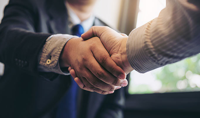 Two individuals wearing smart clothes shaking hands