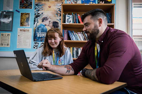 A tutor showing a happy student some information on a laptop