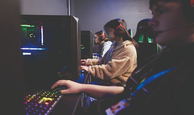 A side shot of three Esports students playing on gaming PC's with colourful equipment surrounding them