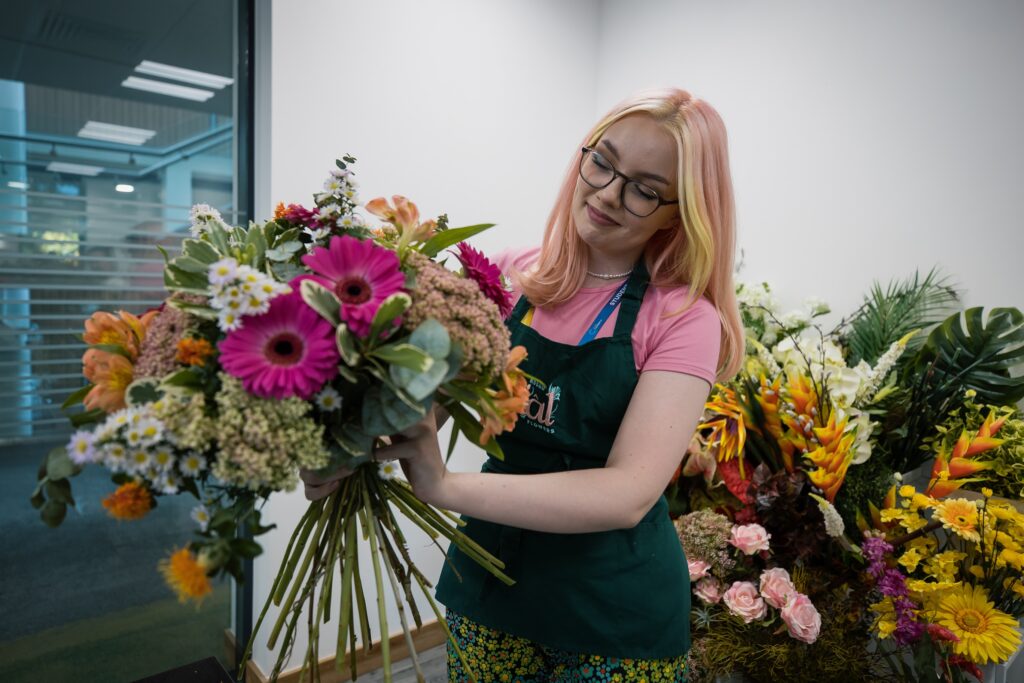 A floristry student arranging a hand-tied bouquet of red and orange flowers