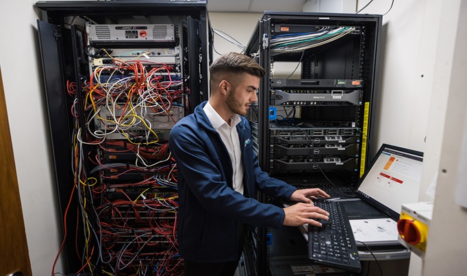 IT Apprentice working on a laptop with servers in the background