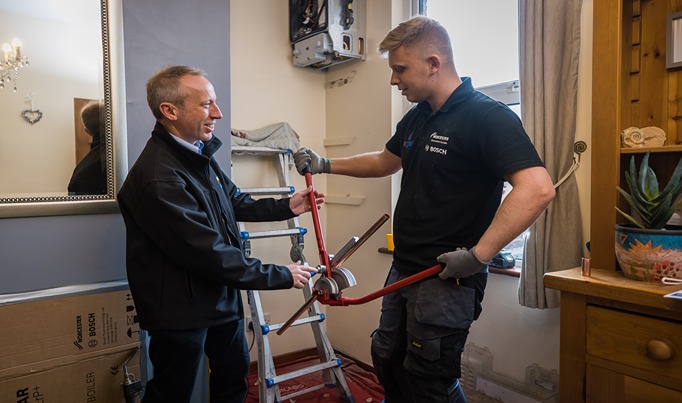 A plumbing apprentice working in a house speaking with an assessor