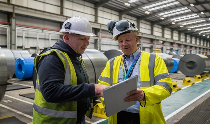 A warehousing apprentice looking at a notebook held by their assessor