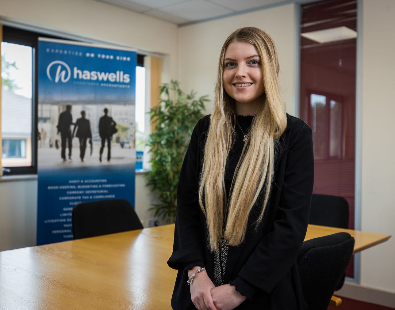 A business apprentice taking a hero shot with a roller banner in the background with her employer 'Haswells' in the background