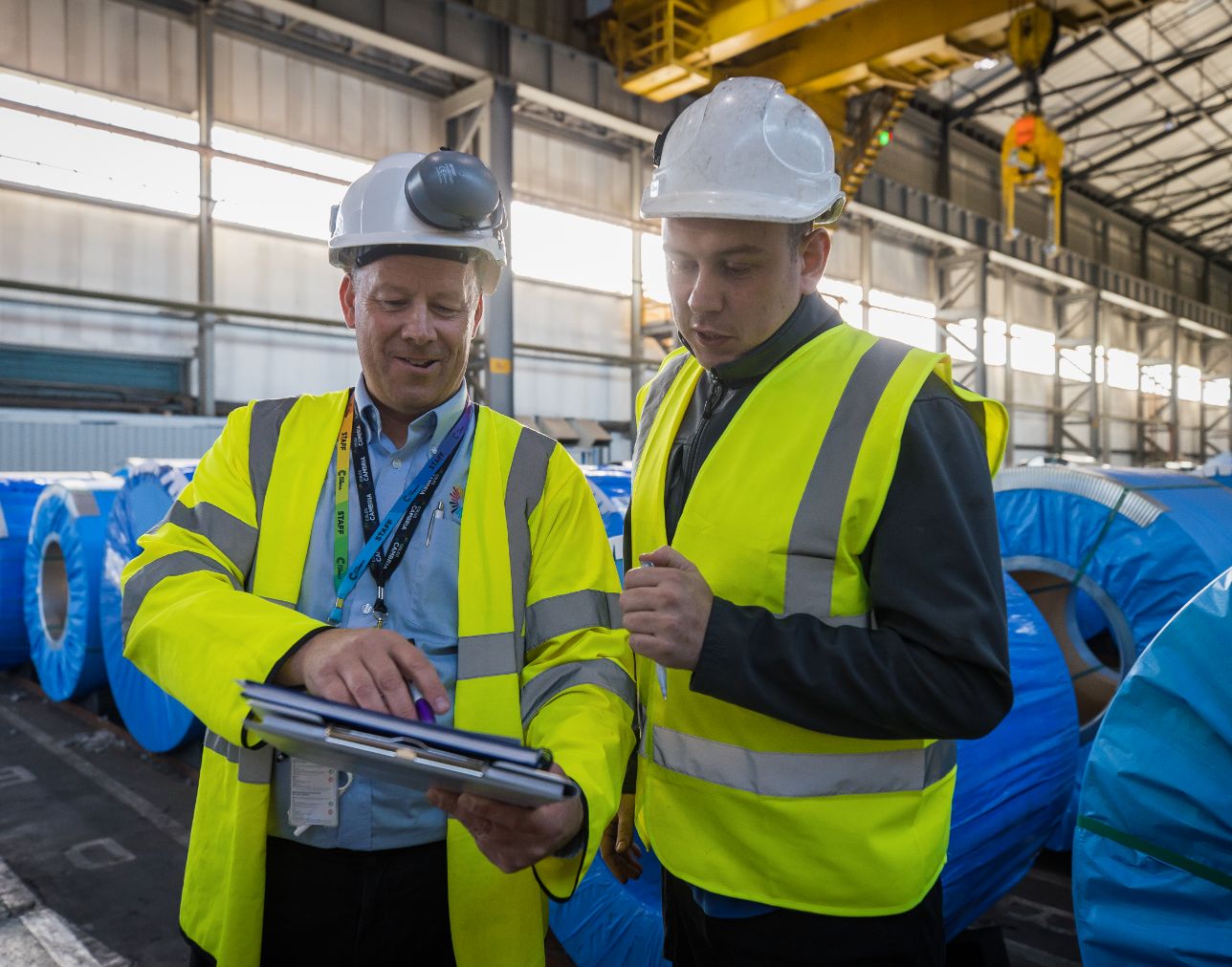 A warehousing apprentice looking at a notebook held by their assessor
