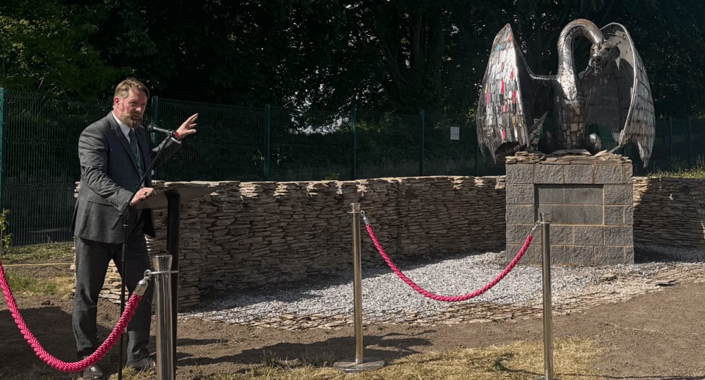 Karl Jackson stood to the left of the photo pointing towards a knife dragon whilst presenting it