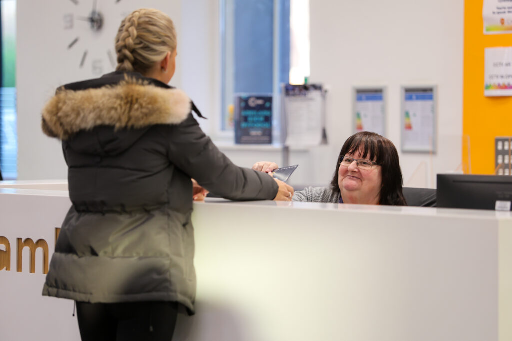 a learner at reception passing an item to the receptionist