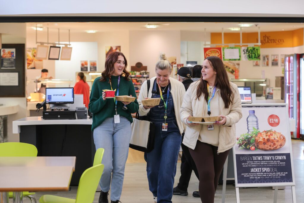 three learners carrying breakfast items in the canteen