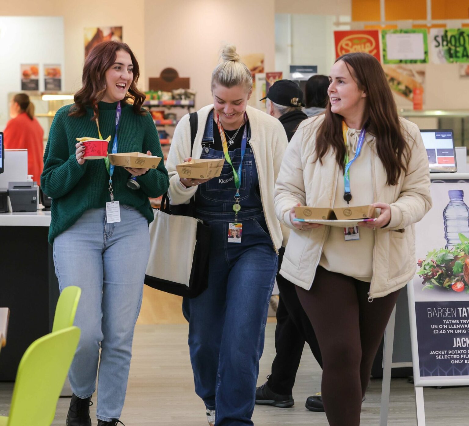 three learners carrying breakfast items in the canteen