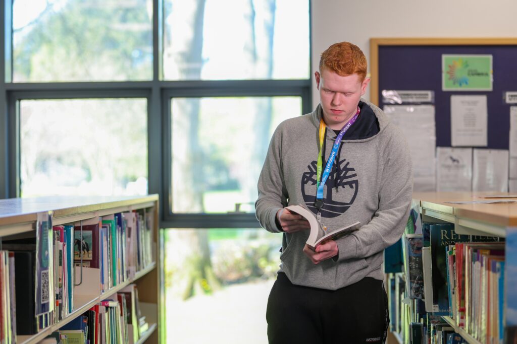 a learner in the library standing up looking at a book