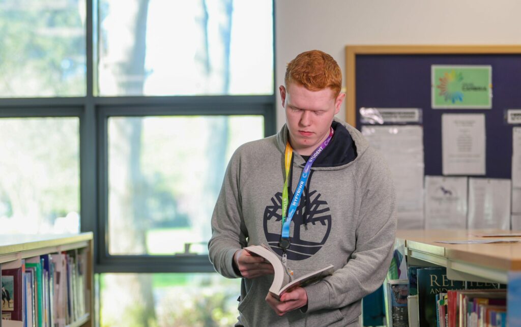 a learner in the library standing up looking at a book